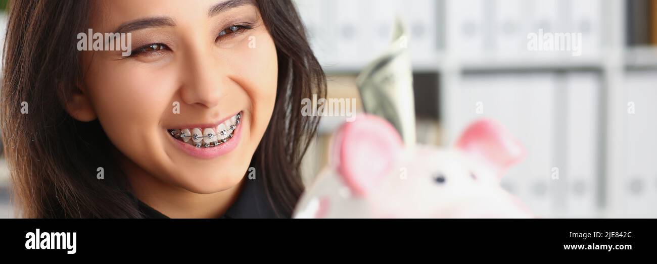 Bella ridendo giovane donna che tiene piggybank con banconota in esso Foto Stock