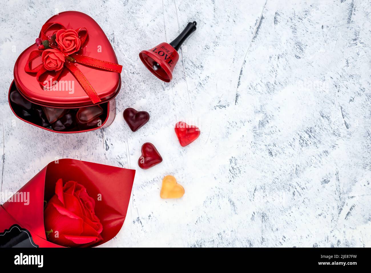 Caramelle gommose a forma di cuore con una scatola regalo in metallo, rosa rossa e campana per San Valentino o Festa della Donna. Vista dall'alto. Foto Stock