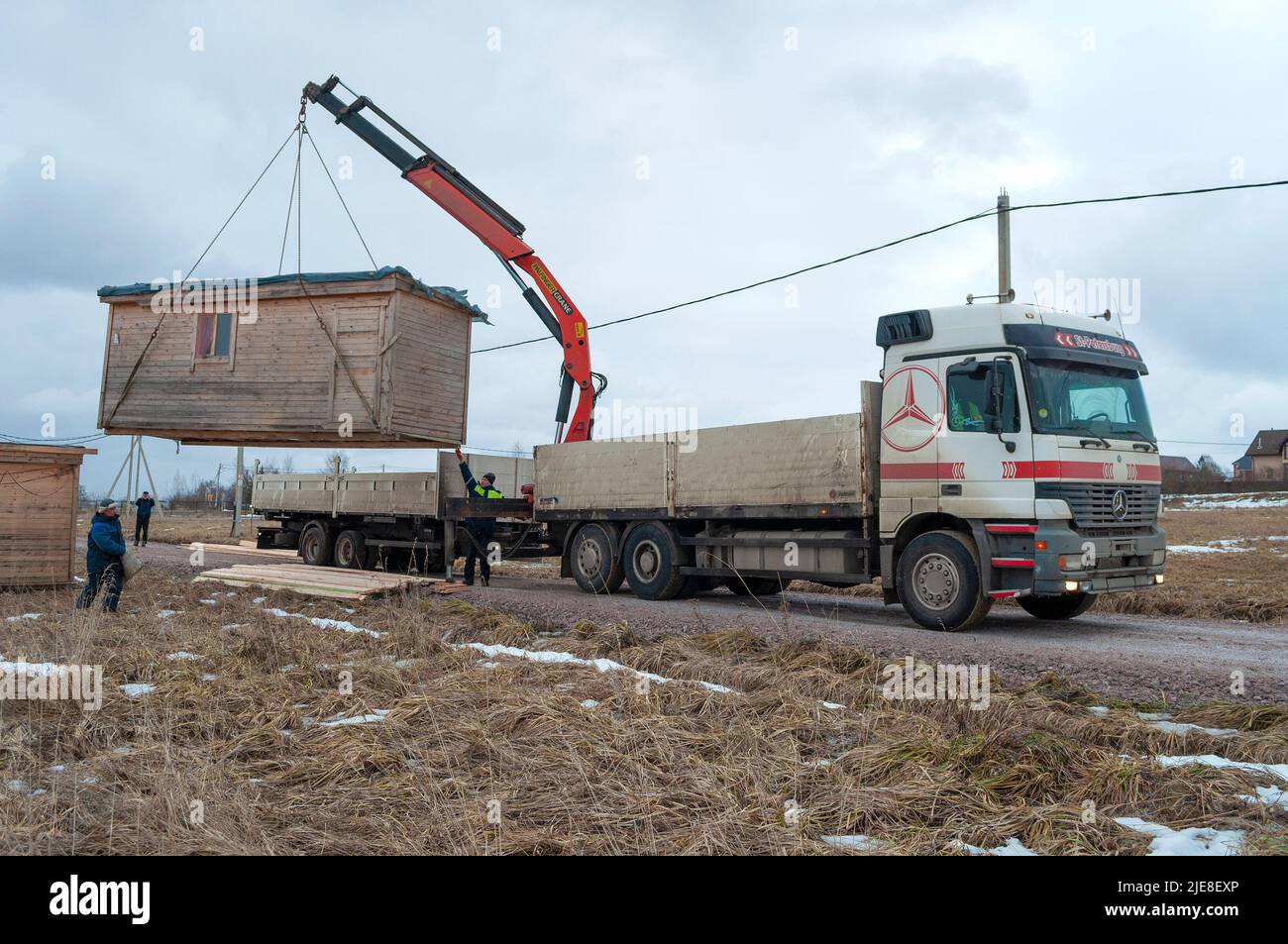 REGIONE DI LENINGRAD, RUSSIA - 04 MARZO 2021: Un camion con una gru manipolatrice scarica un capannone di costruzione in una nuvolosa giornata di marzo Foto Stock