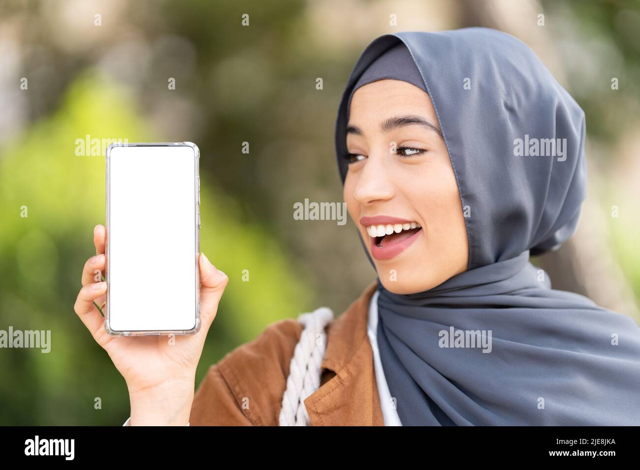 Donna musulmana amichevole che mostra lo schermo del mobile Foto Stock