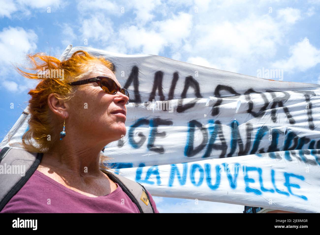 Una donna con i capelli che soffiano nel vento di fronte a una bandiera, Mirage Dangereux a Port la Nouvelle. Manifestazione regionale contro il GPII (grandi progetti inutili e imposti). Autostrade, superstrade, allevamenti industriali di bestiame, dighe, piattaforme logistiche, Insane attività forestali, fotovoltaici e parchi eolici industriali, riapertura delle miniere, ampliamento di un porto, complesso immobiliare e il suo campo da golf, LGV, verruche urbane, mega trasformatore con le sue linee VHT, dispiegamento del 5G e la sua tecnologia digitale distruttiva. Francia, Tolosa il 25 giugno 2022. Foto di Patricia Huchot-Boissier/ABACAP Foto Stock