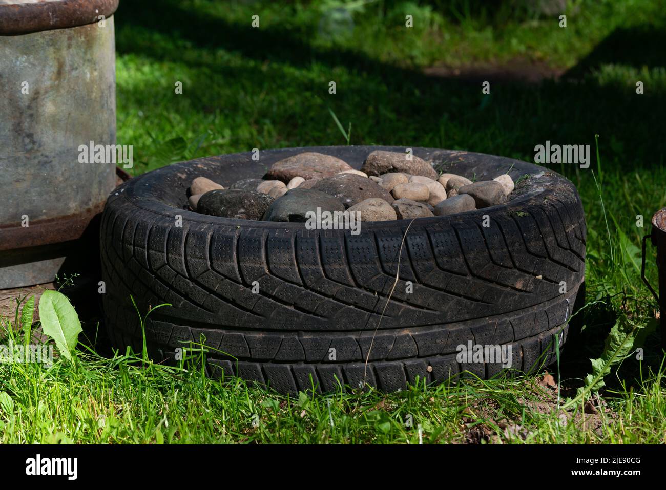 Il pneumatico auto nella foresta in erba verde è caricato pieno di ciottoli di pietra. Natura sporca Foto Stock