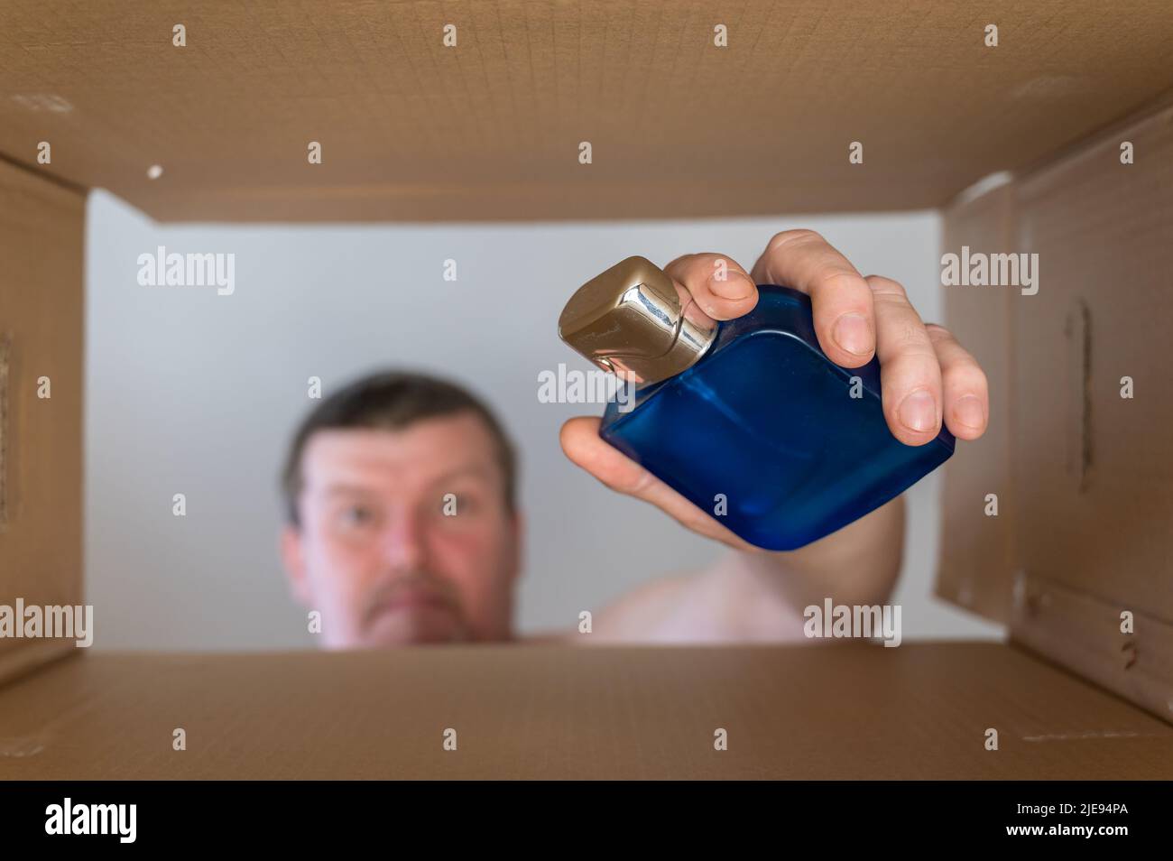 Un uomo estrae il profumo da una scatola mobile di cartone. Bottiglia di profumo in vetro blu con tappo in argento. Vista dal basso. Vista interna. Primo piano. Messa a fuoco selettiva Foto Stock