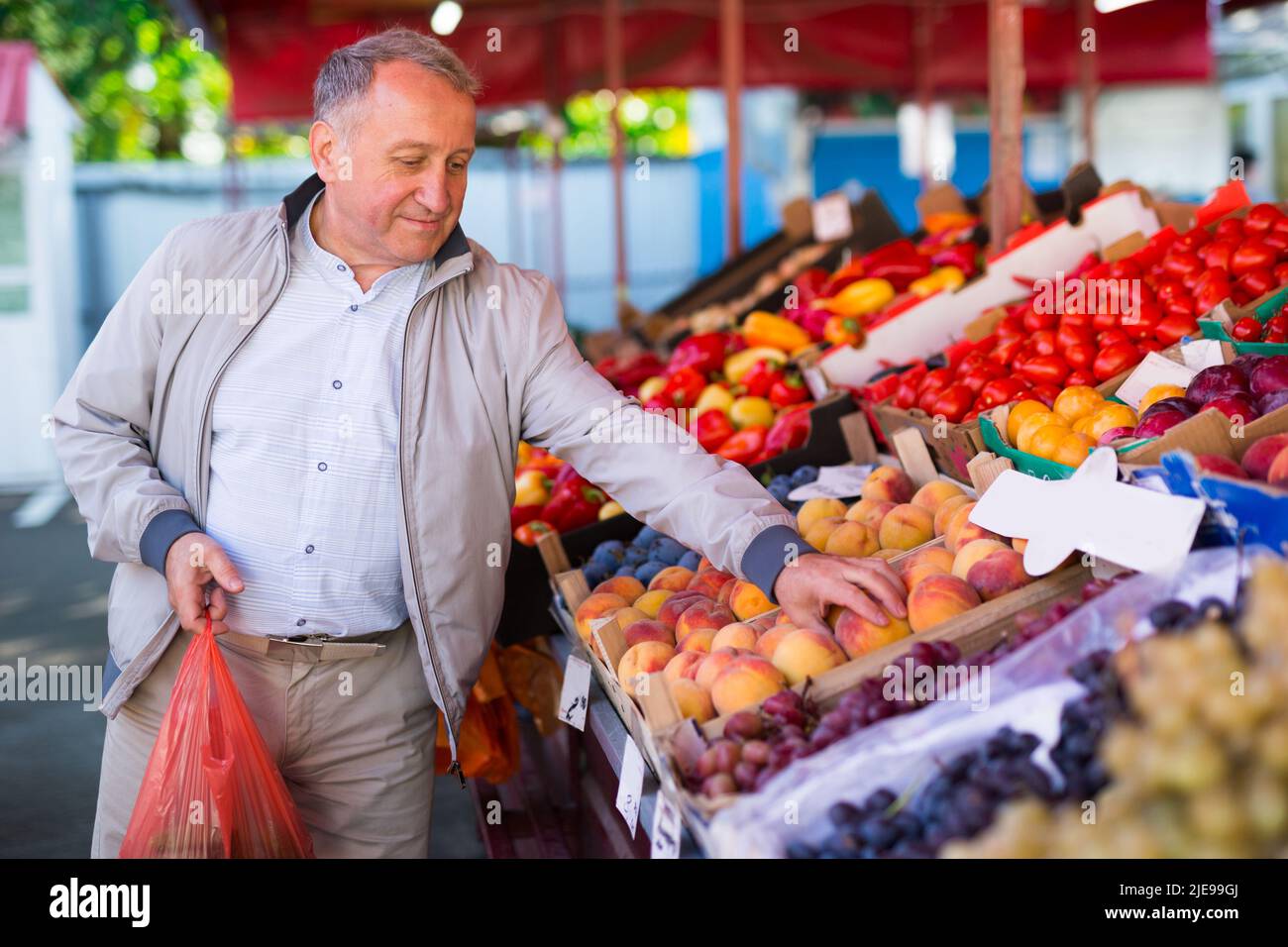 Uomo che sceglie le pesche nel mercato Foto Stock