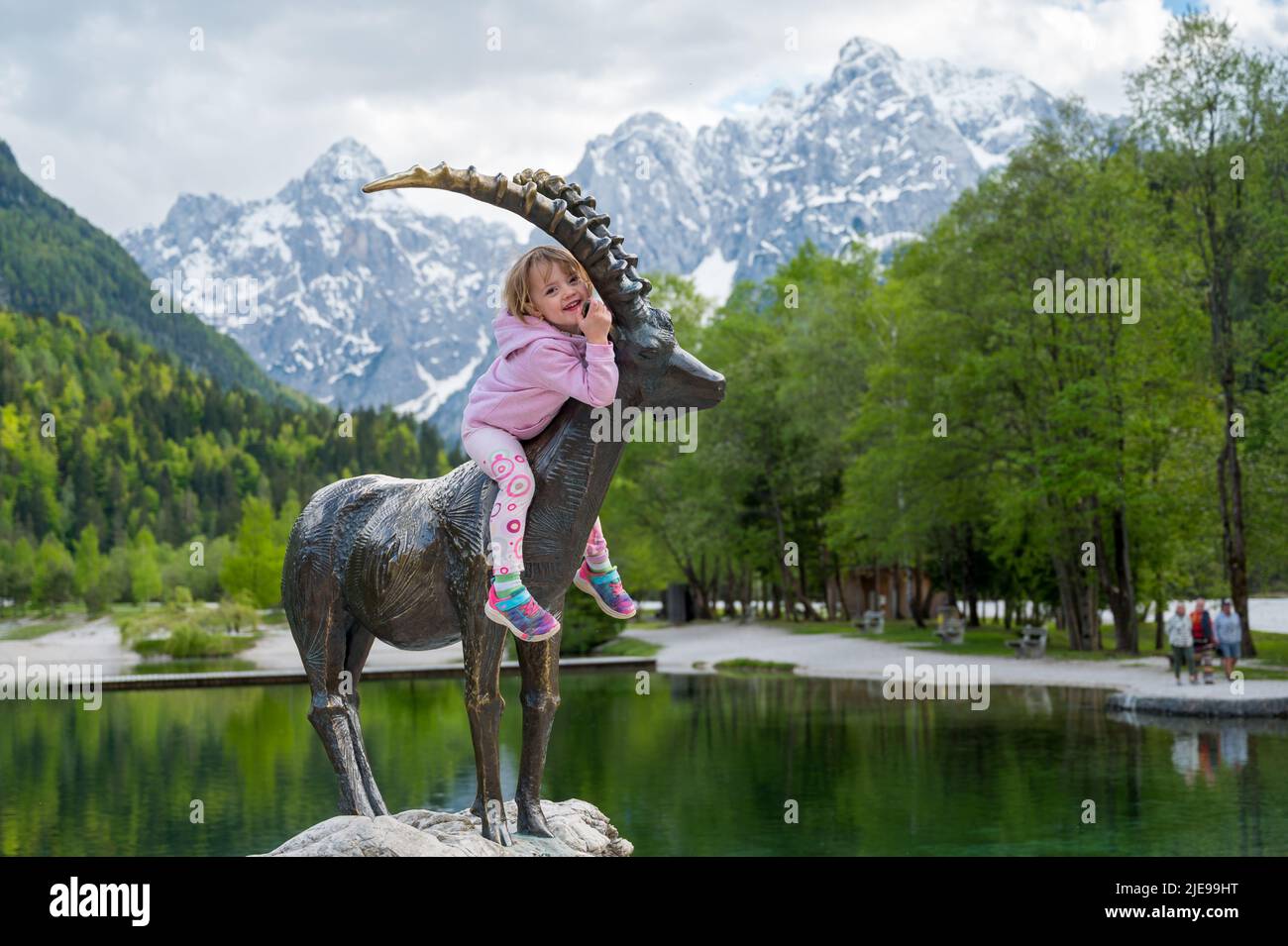 Ragazza bionda carina in sella a una statua stambecco con paesaggio di montagna. Foto Stock