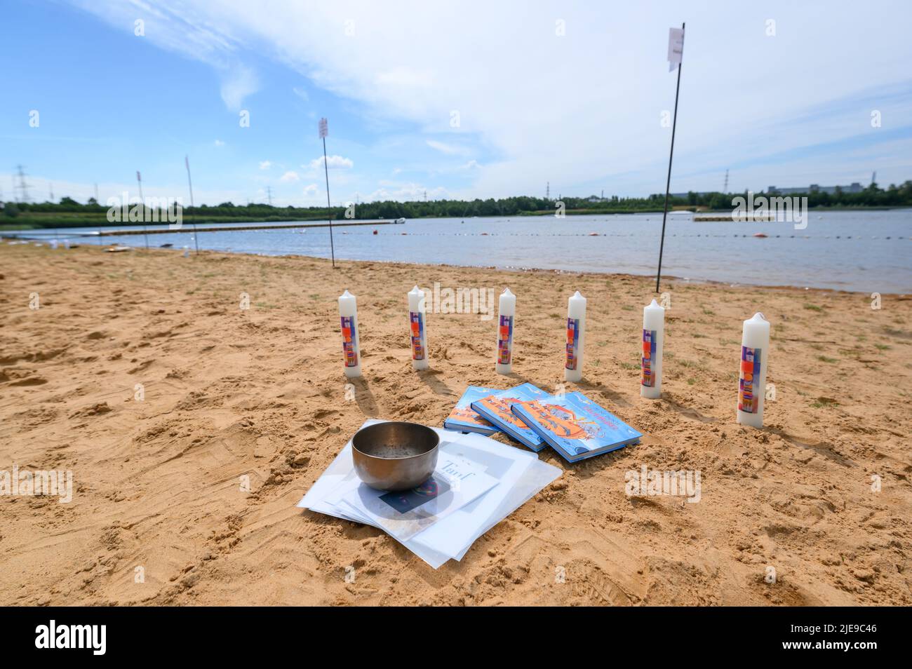 Norderstedt, Germania. 26th giugno 2022. Candele battesimali, libri e una ciotola di metallo si trovano sulla spiaggia sulla riva dello Stadtparksee prima della cerimonia del battesimo. Un battesimo di massa con 57 partecipanti e circa 500 ospiti è stato celebrato da sette congregazioni della chiesa nello Stadtparksee di Norderstedt, vicino Amburgo. Credit: Jonas Walzberg/dpa/Alamy Live News Foto Stock