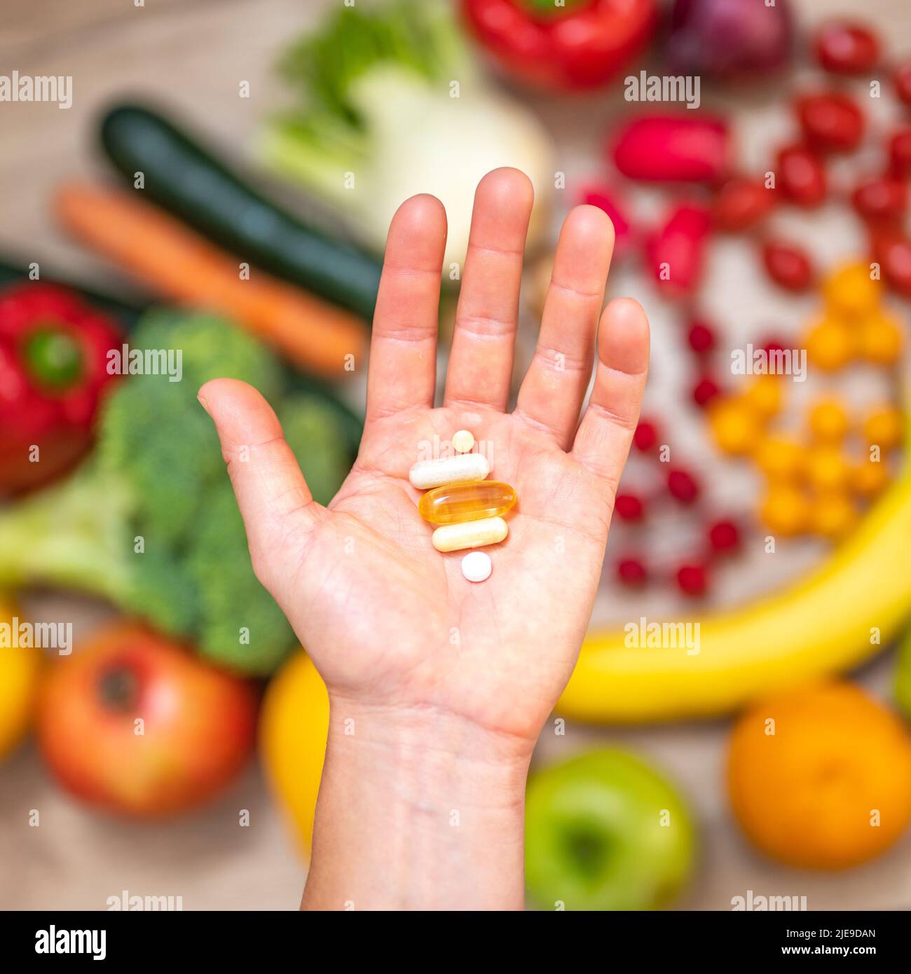 Mano sta tenendo le tovlette di supplemento di cibo sopra una tabella di legno piena di verdure e frutta. Gli integratori alimentari consentono uno stile di vita sano. Foto Stock