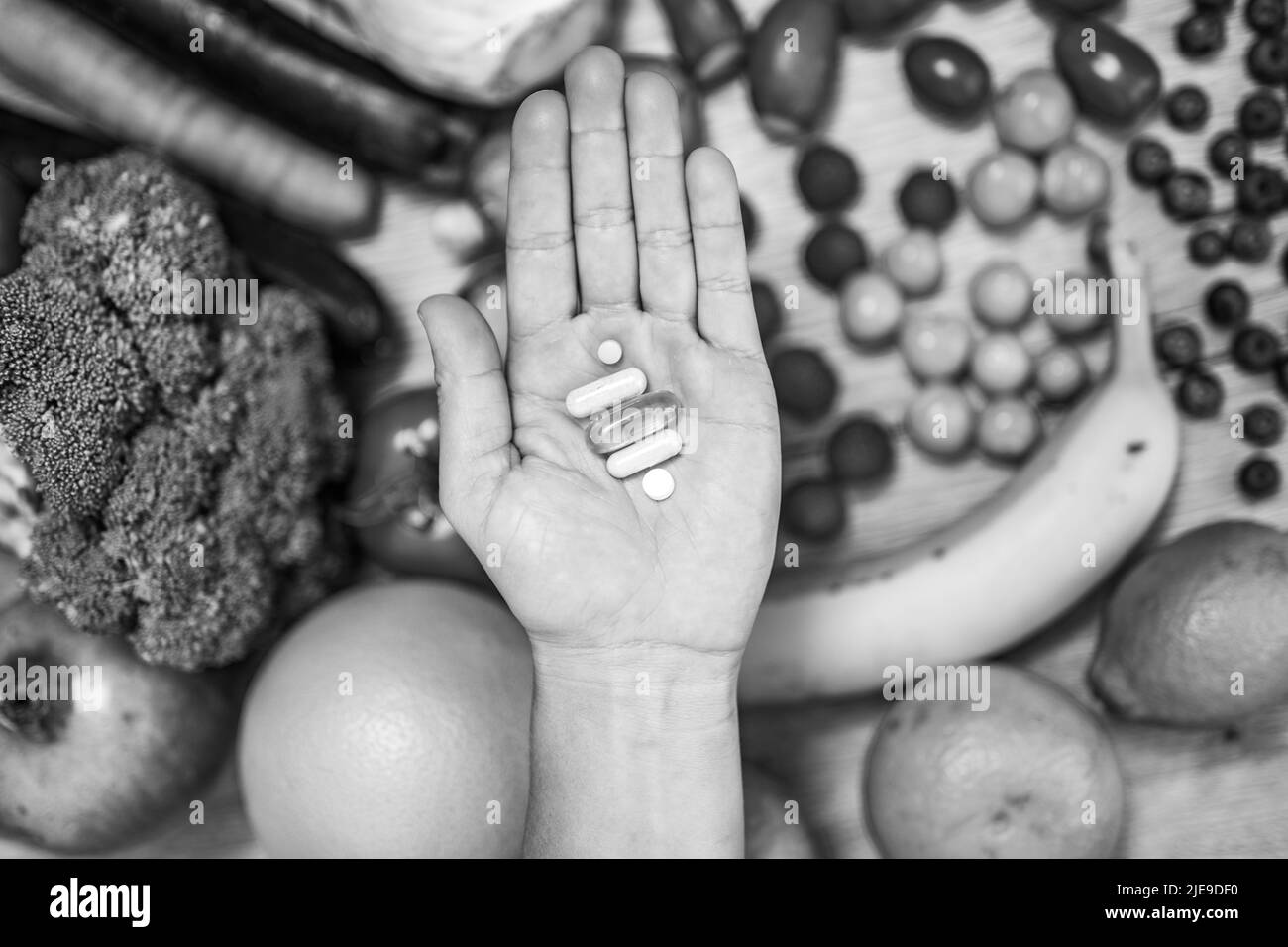 Mano sta tenendo le tovlette di supplemento di cibo sopra una tabella di legno piena di verdure e frutta. Gli integratori alimentari consentono uno stile di vita sano. Foto Stock