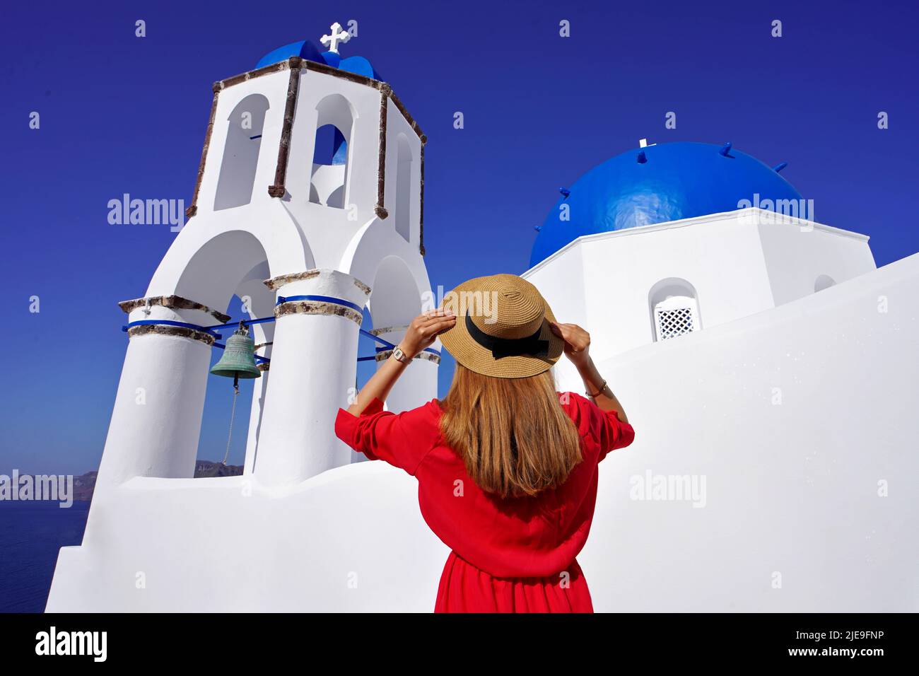 Vacanze in Grecia. Ragazza viaggiatore che tiene cappello godendo di vista delle famose cupole blu di Santorini chiese imbiancate. Foto Stock