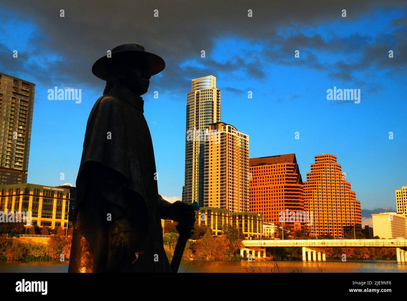 Una statua di scultura di rock and roll musicista e chitarrista Stevie Ray Vaughn si erge in silhouette contro lo skyline di Austin, Texas Foto Stock