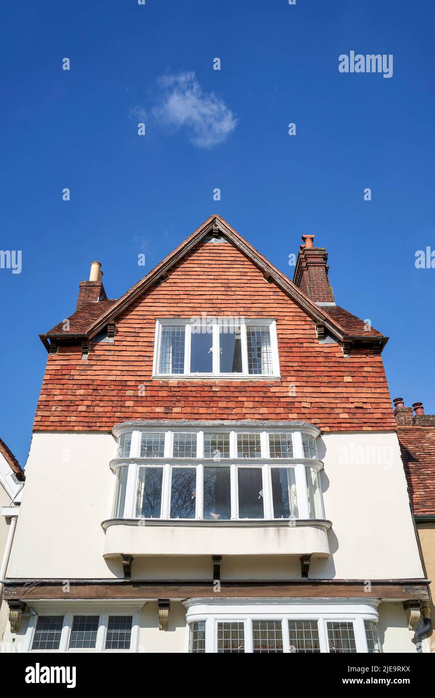 Guardando in su ad una casa alta con il rivestimento appeso delle mattonelle di argilla e la finestra della baia sotto cielo blu sopra con la piccola nuvola singola Foto Stock