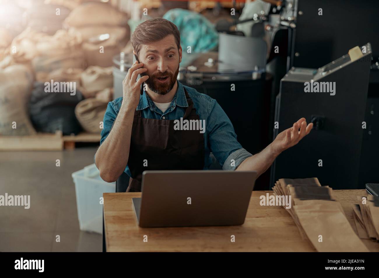 Il proprietario di affari che parla con il cliente mentre siede nella propria piccola fabbrica di caffè Foto Stock