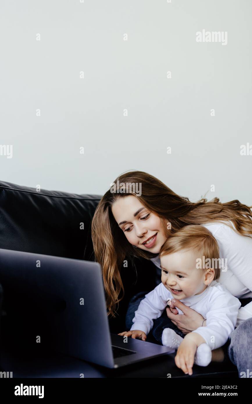 un freelance sorridente che punta al laptop mentre tiene un figlio piccolo Foto Stock