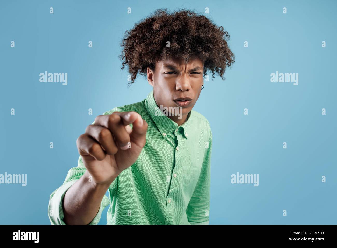 Il giovane ragazzo africano ameriano guarda qualcosa sullo schermo virtuale e si avvicina, in piedi su sfondo blu studio Foto Stock