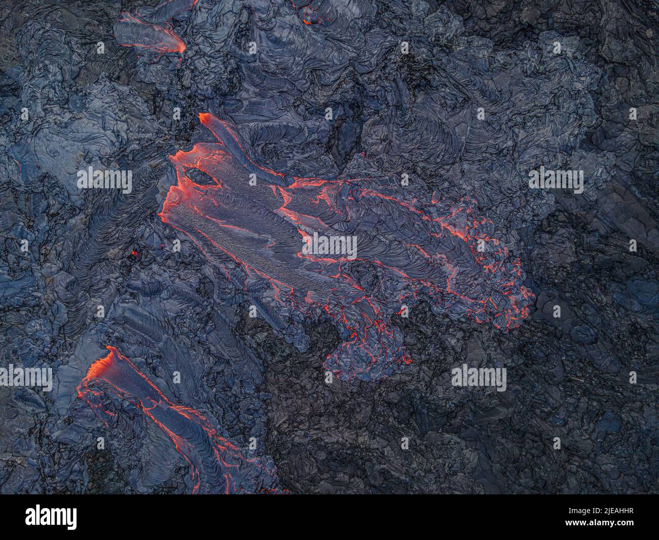 Flusso di lava dall'alto. La magma calda rossa scorre da un vulcano attivo sulla penisola islandese di Reykjanes. Strutture nella roccia blu-nera. Magm raffreddato scuro Foto Stock