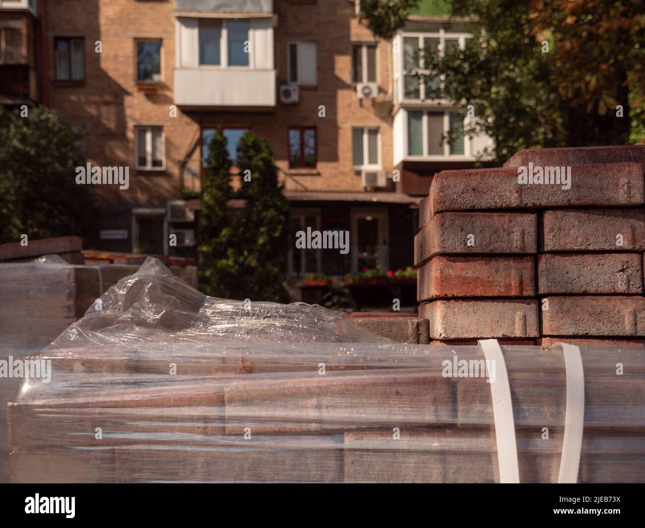 Una pila di piastrelle di pavimentazione e un pacco di sigarette in primo piano e un vecchio edificio di mattoni rossi illuminato dal sole sullo sfondo a Kiev, Ucraina. Foto Stock