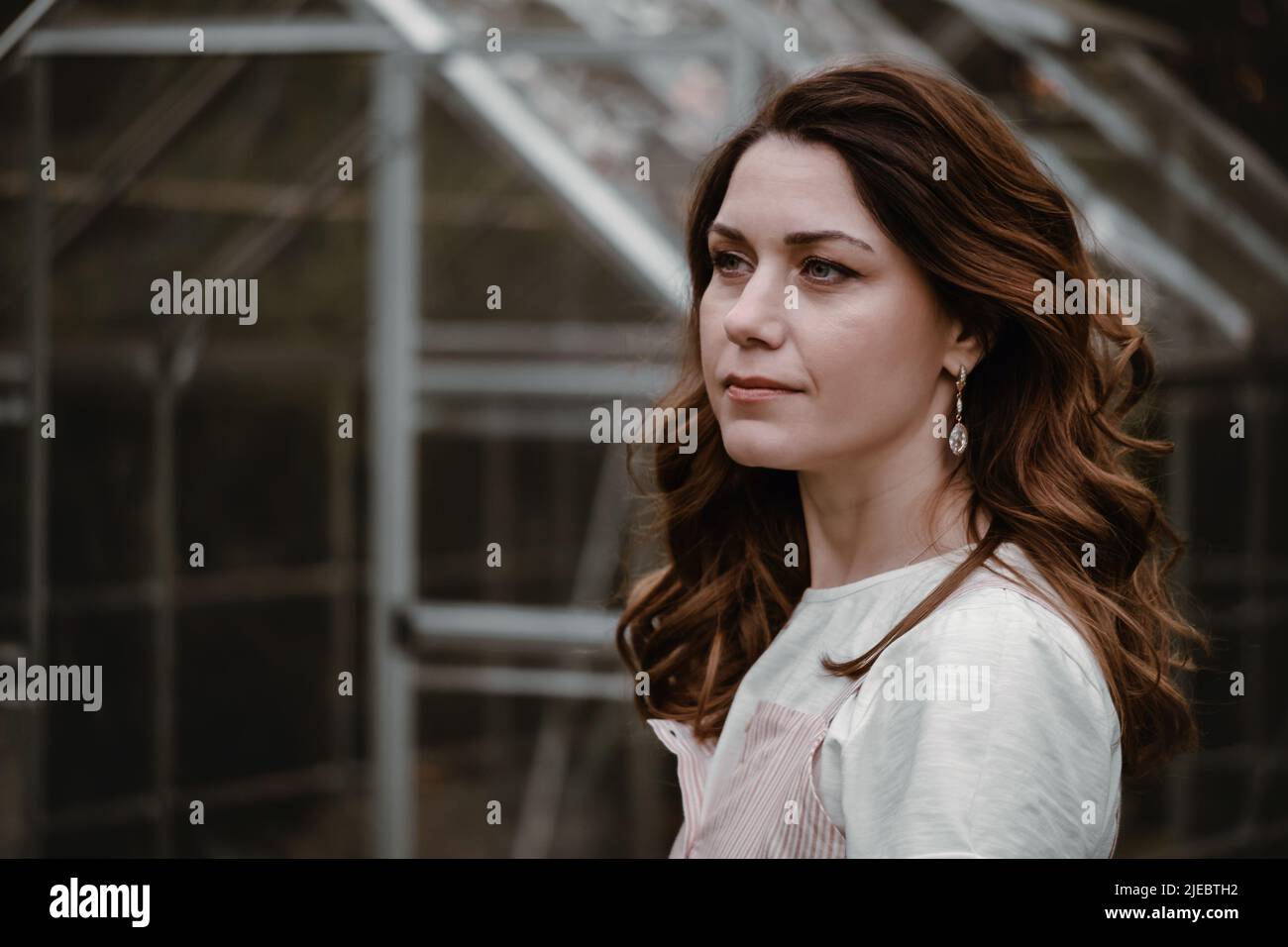 Bella donna al suo 30s nel giardino sera scuro. Bella donna ricci da sogno in serata camminando in abito lungo sopra serra. Moda Foto Stock