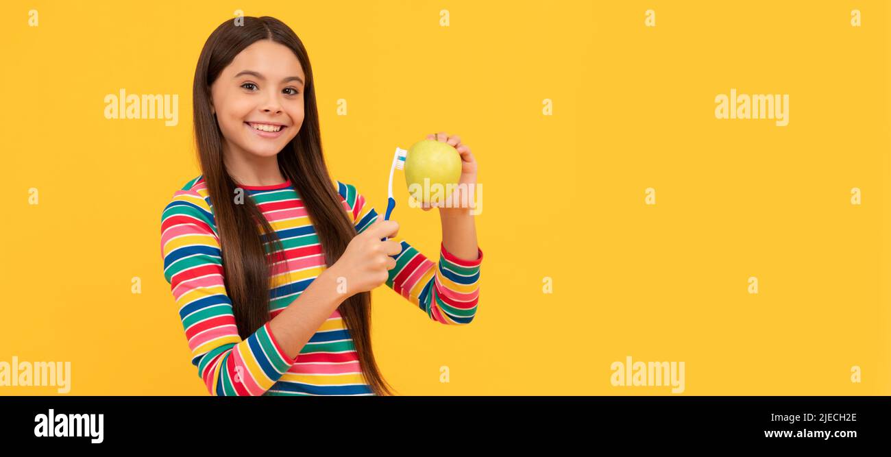 Felice ragazza bambino spazzolare mela con spazzolino sfondo giallo, igiene orale. Banner di bambina con spazzola dentaria, ritratto studio, intestazione con copia Foto Stock