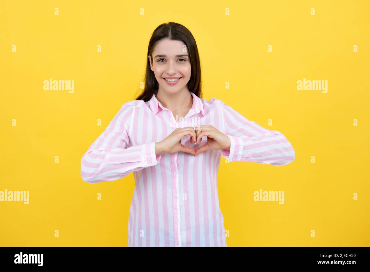 Giovane donna piuttosto romantica che fa un gesto di cuore, mostrando amore e affetto riconoscente gesto con un felice sorriso tenero. Ragazza sentimenti amore. Incantevole Foto Stock