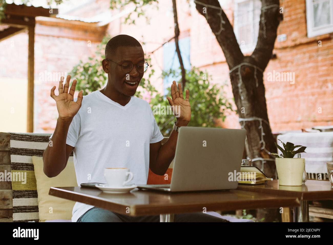Closeup sorridendo l'uomo d'affari afroamericano che lavora sul laptop, sollevando le armi come difesa e guardando monitor. Webinar Foto Stock