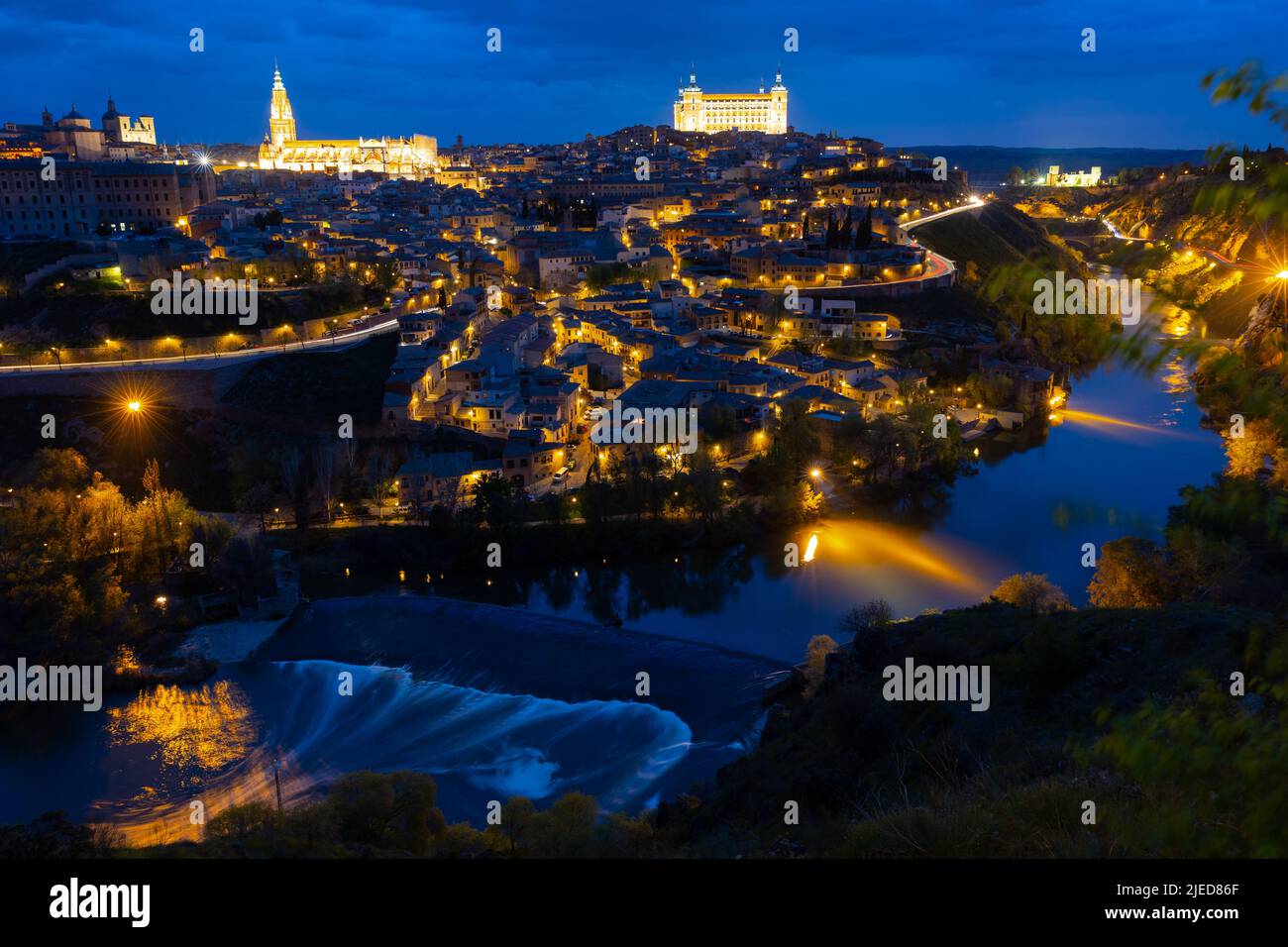 Paesaggio urbano di Toledo illuminata di sera con vista sul fiume Tago Foto Stock