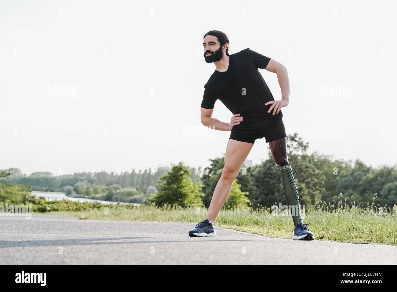 Adatta l'uomo con disabilità fisica facendo il riscaldamento stretching prima della routine di esercizio all'aperto - concentrarsi sulla gamba protesica Foto Stock