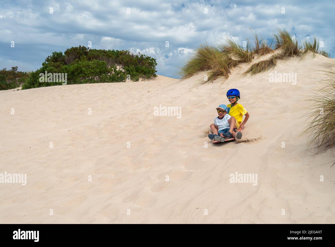 I bambini si divertono mentre scivolano giù una duna di sabbia su una tavola da sabbia, Kangaroo Island, South Australia Foto Stock