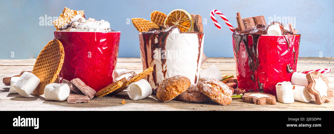 Tazze di cioccolato caldo in stile natalizio con vari condimenti: Fette di cioccolato, spezie, dolci, biscotti, caramelle e pani di zenzero, accogliente in legno Foto Stock