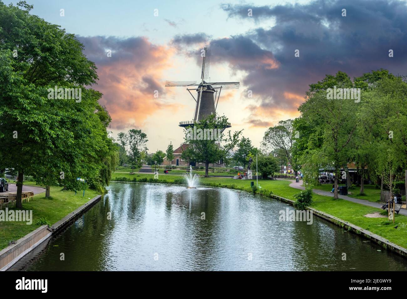 Mulino dei Paesi Bassi. Molen De Valk è un mulino a torre e museo nella città di Leiden, in Olanda. Riflessi sull'acqua del canale, cielo nuvoloso blu al tramonto Foto Stock