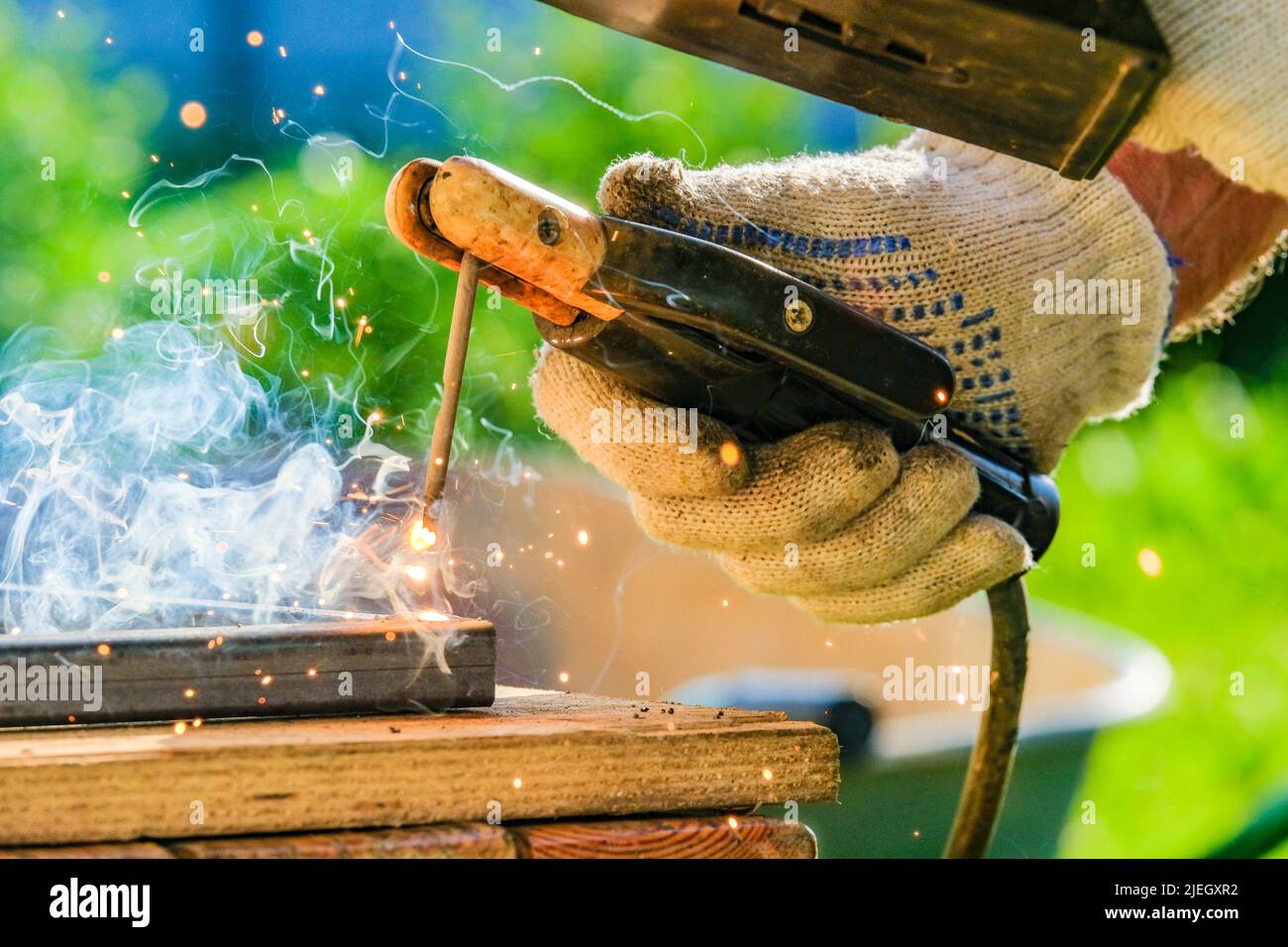 Fuoco selettivo su un elettrodo caldo in mano a una saldatrice che saldano tubi metallici. Scintille e fumo dalla saldatura ad arco di metallo. Foto Stock