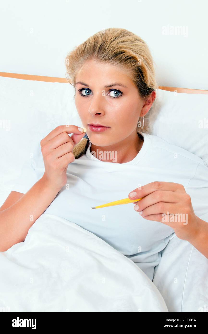 Eine Frau im Bett ist Krank und Hat ein Fiebertermumer in der hand Foto Stock