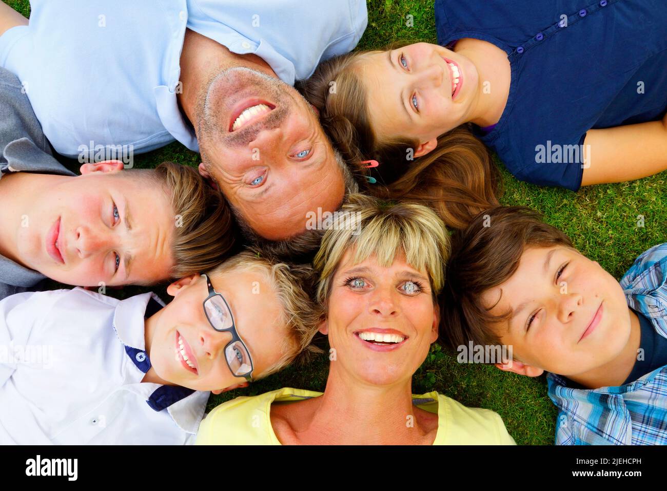 Familie liegt mit dem Rücken auf den Rasen und blickt in den Himmel, 6 Personen, Mann, Frau, Tochter, 3 Jungen, Foto Stock