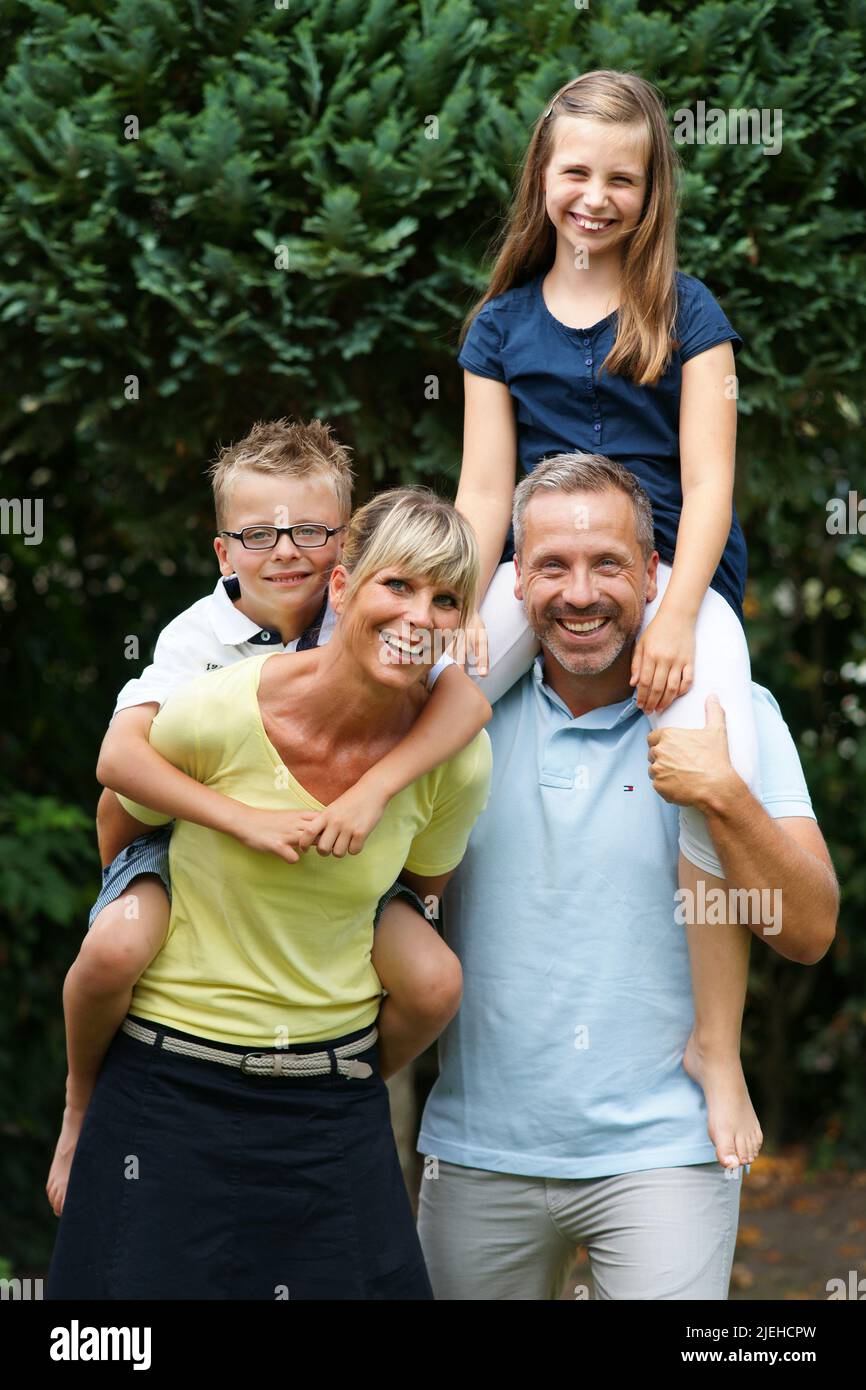Eine glückliche Familie im Garten, 4 Personen, Eltern nehmen die Kinder Huckepack, Foto Stock