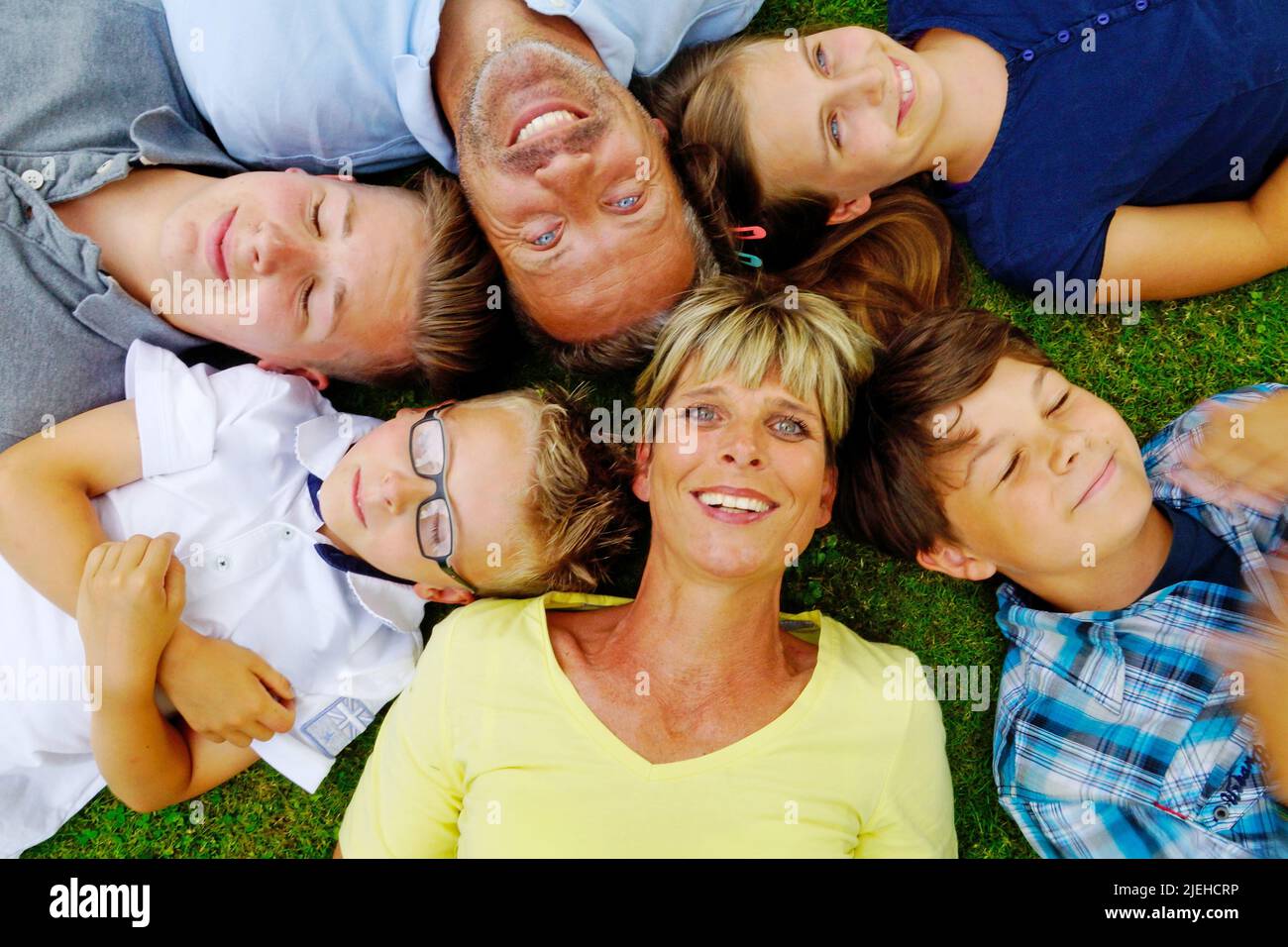Familie liegt mit dem Rücken auf den Rasen und blickt in den Himmel, 6 Personen, Mann, Frau, Tochter, 3 Jungen, Foto Stock