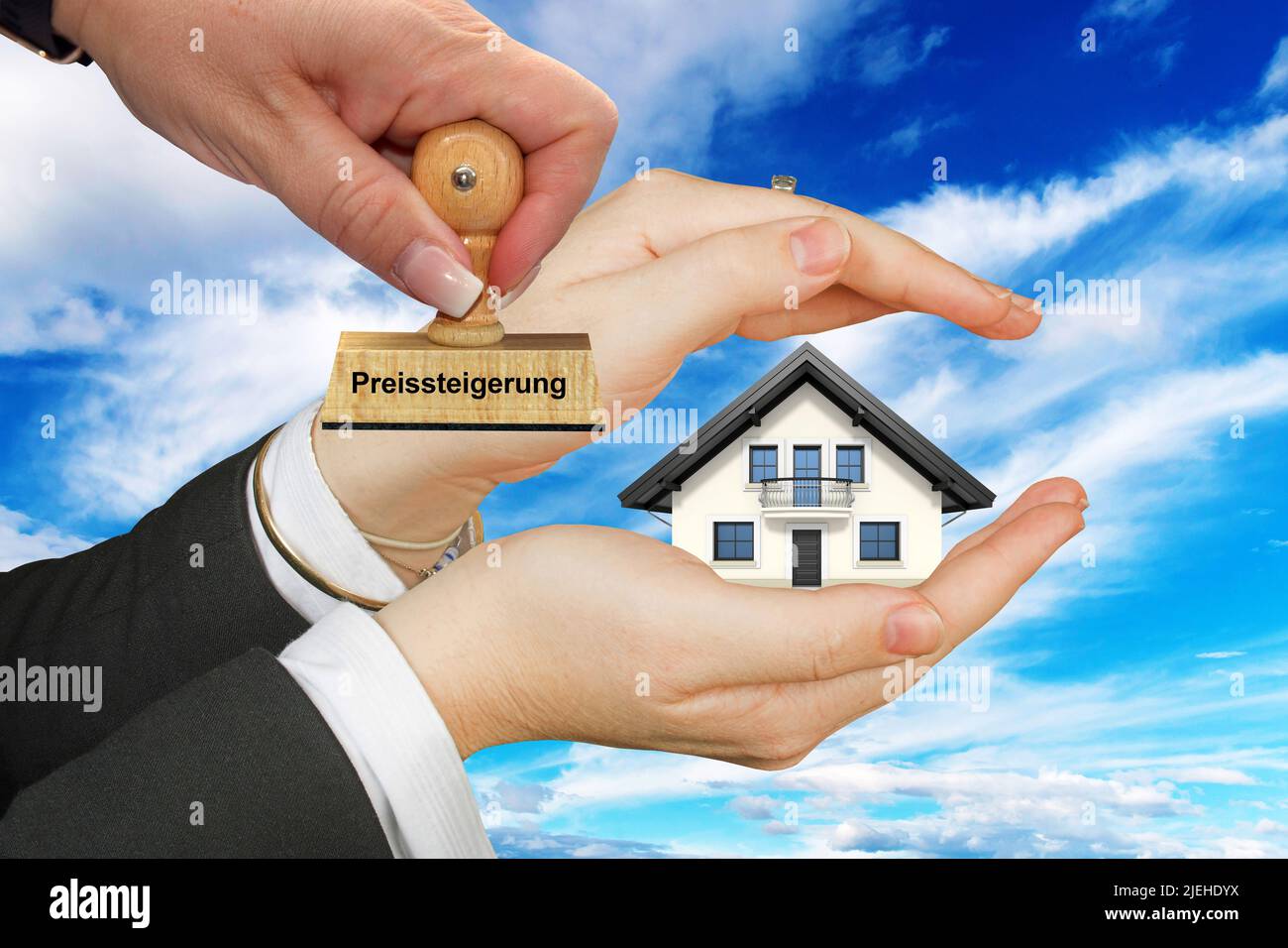 Immobilien werden teurer, Schützende hand mit Einfamilienhaus, Freisteller, weisser Hintergrund, Wolkenhimmel, Frauenhand, Preisteigerung, Foto Stock