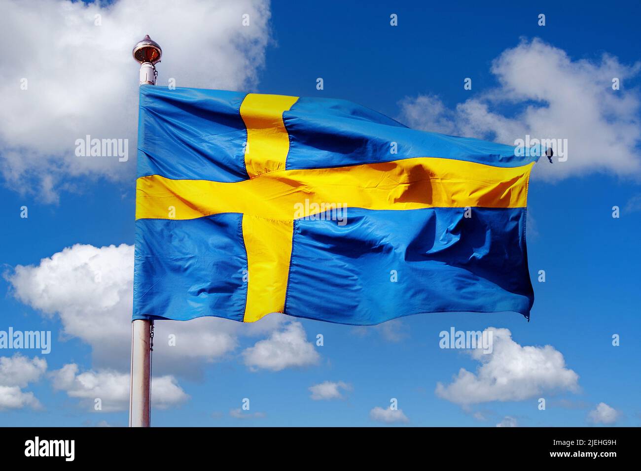 Die Nationalfahne von Schweden vor blauen Himmel mit Cumuluswolken Foto Stock