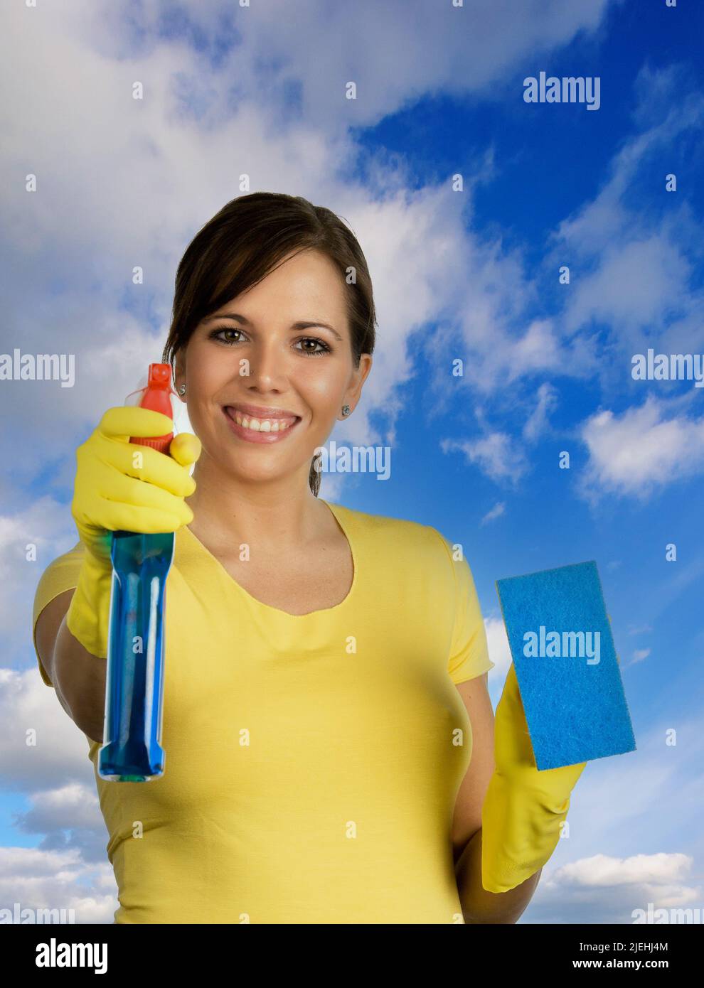 Junge Frau mit Reinigungsmittel putzt eine Fensterscheibe von aussen, durcvh die Scheibe fotografiert, blauer Himmel, Foto Stock