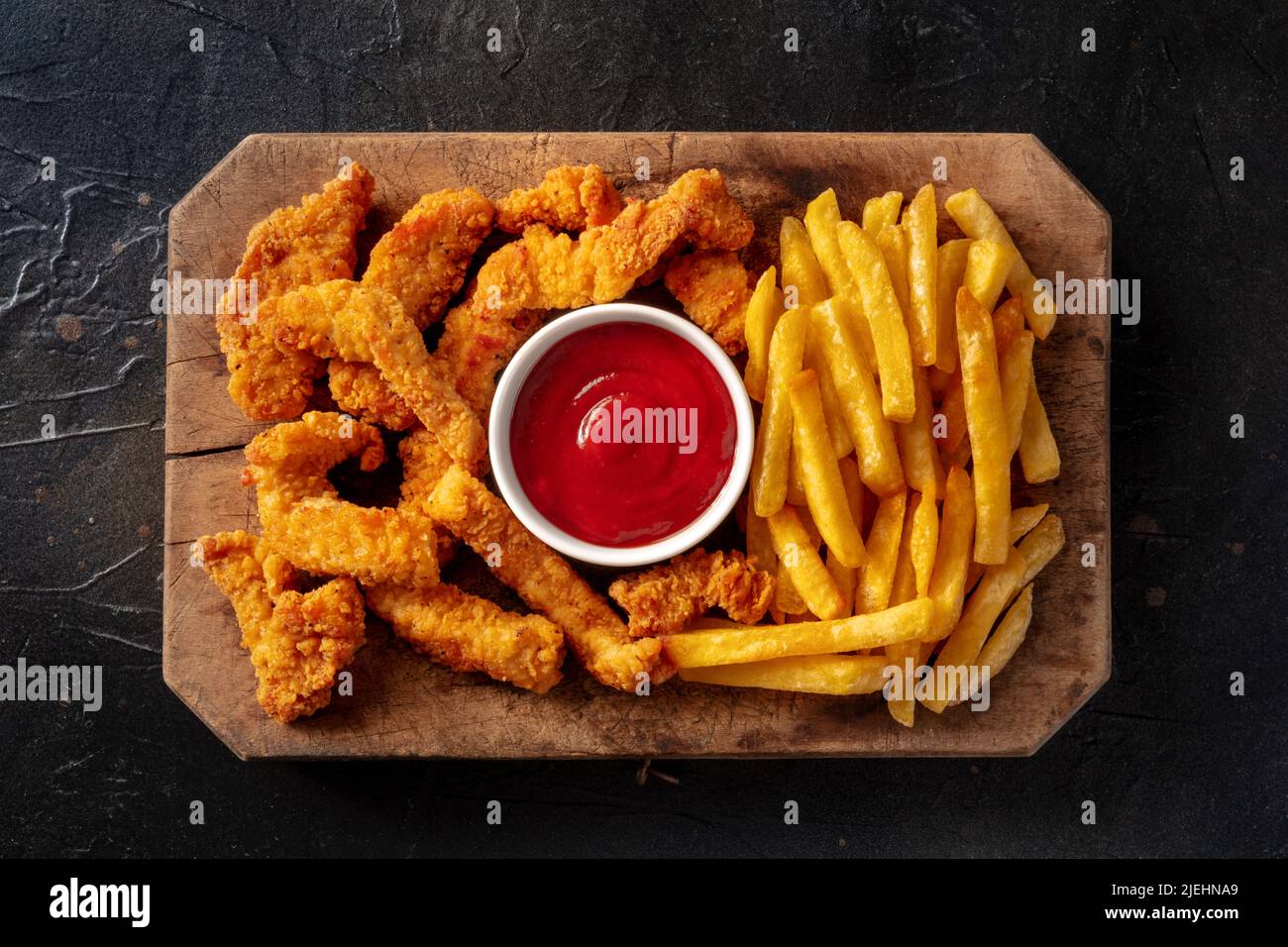 Aste di pollo, pezzi di carne disossati croccanti, con un tuffo rosso e patatine fritte, piatto sopra un colpo di ardesia nero fondo Foto Stock