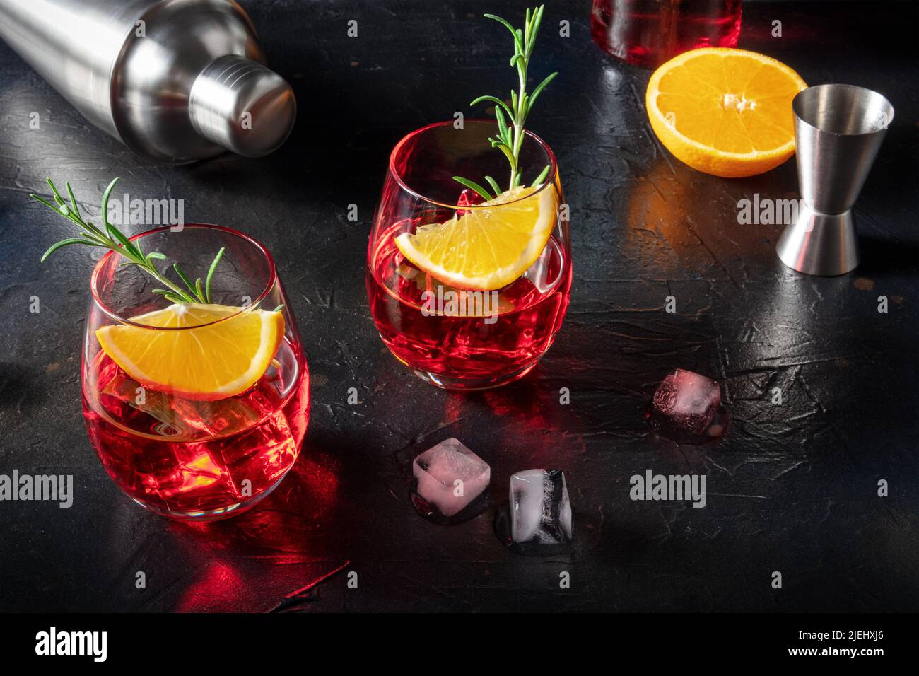 Cocktail Negroni con campari, arance fresche, rosmarino, shaker e jigger, su sfondo scuro con un posto per il testo Foto Stock