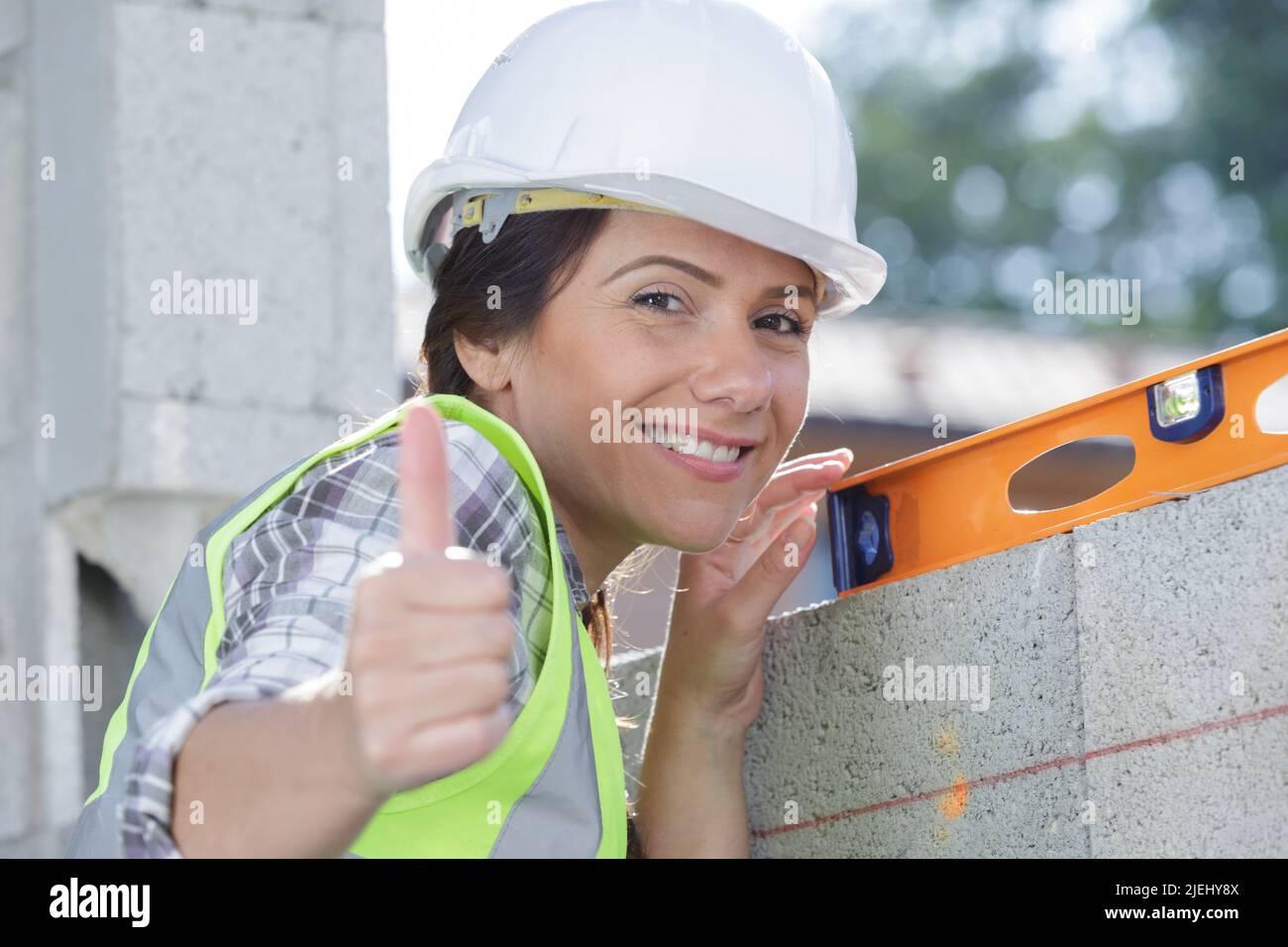 felice costruttore femminile con un livello mostra pollice-su Foto Stock