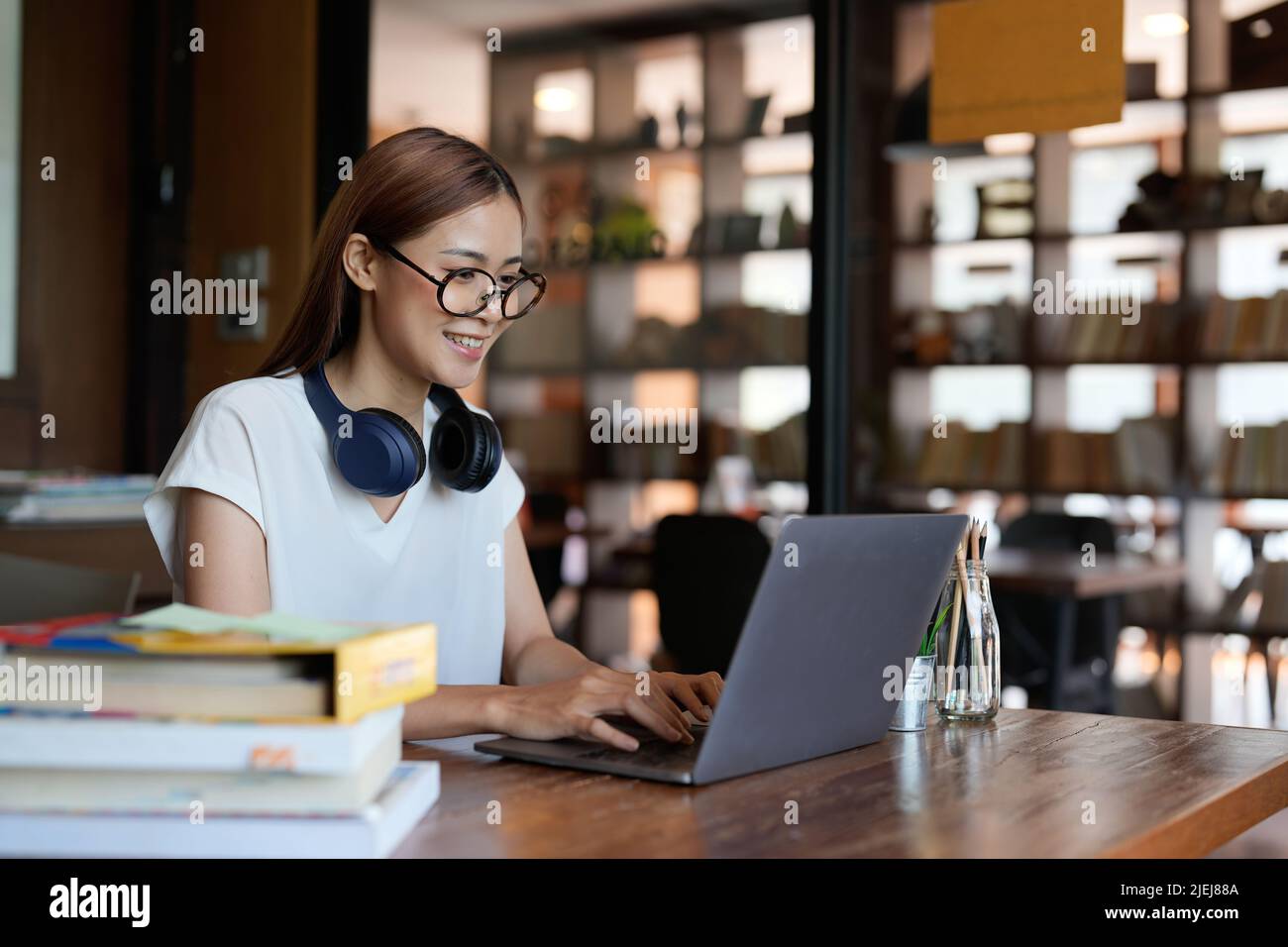 Sorridente adolescente asiatico con cuffie che guarda lo schermo del laptop ascoltare e imparare corsi online. Felice donna cinese d'affari con cuffie video Foto Stock