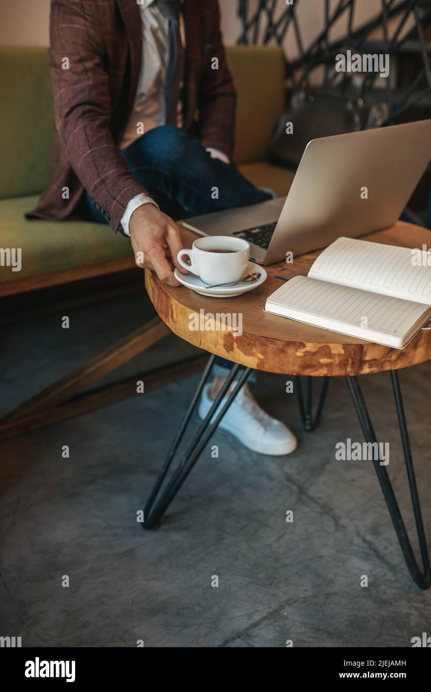 Maschio mano che tocca il caffè sul tavolo vicino al computer portatile Foto Stock