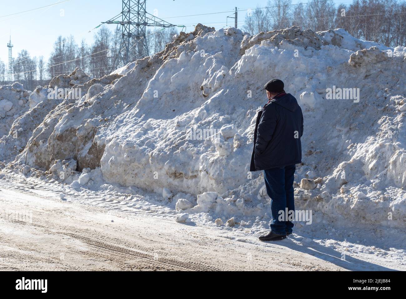 Un uomo in piedi accanto ad un grande cumulo di neve sul lato della strada. Alte nevicate dopo una nevicata o una bufera. Sgombrare la neve sulle strade per garantire una dri sicura Foto Stock