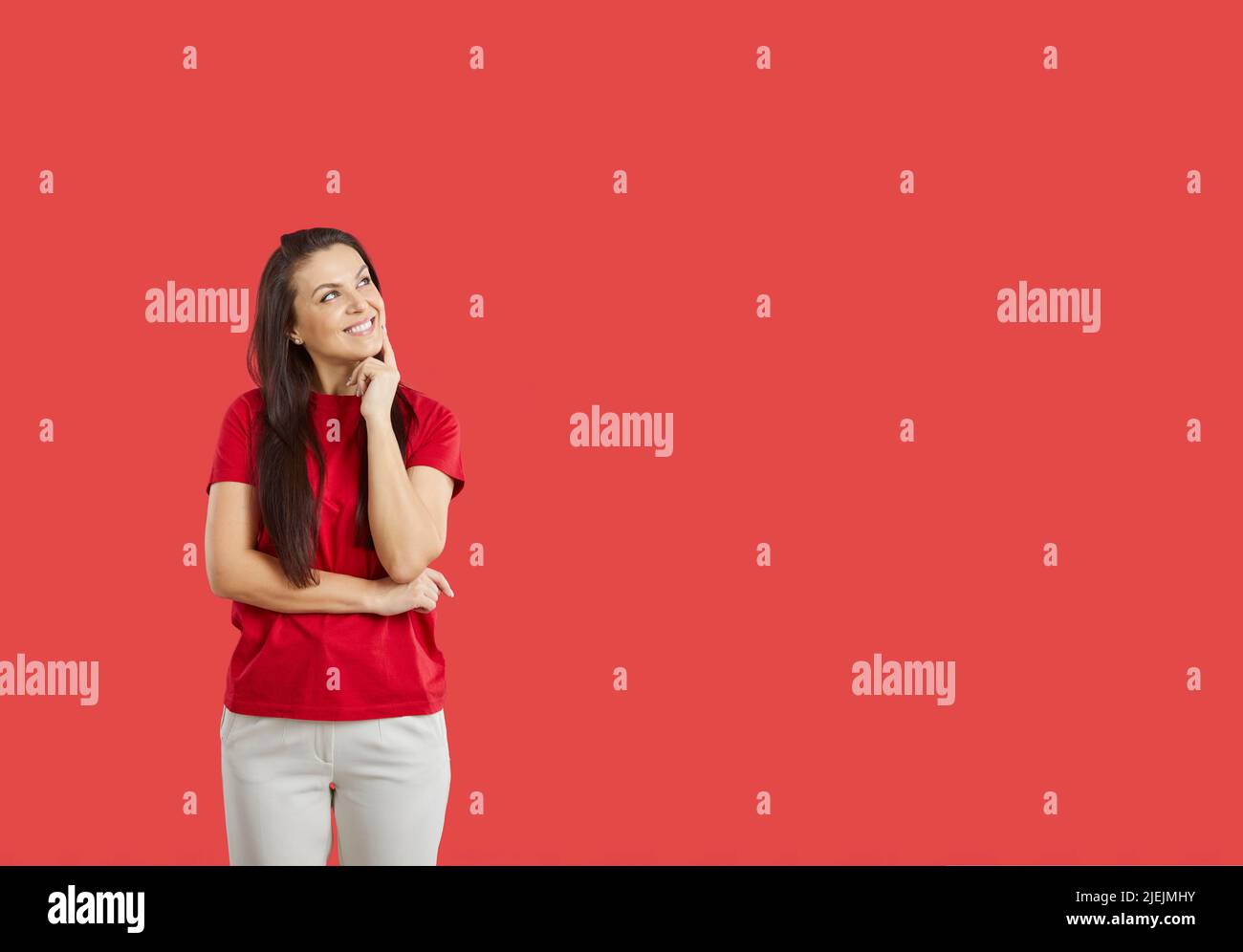 Donna sorridente carina su sfondo rosso ponder, immagina o arriva con qualcosa di interessante. Foto Stock