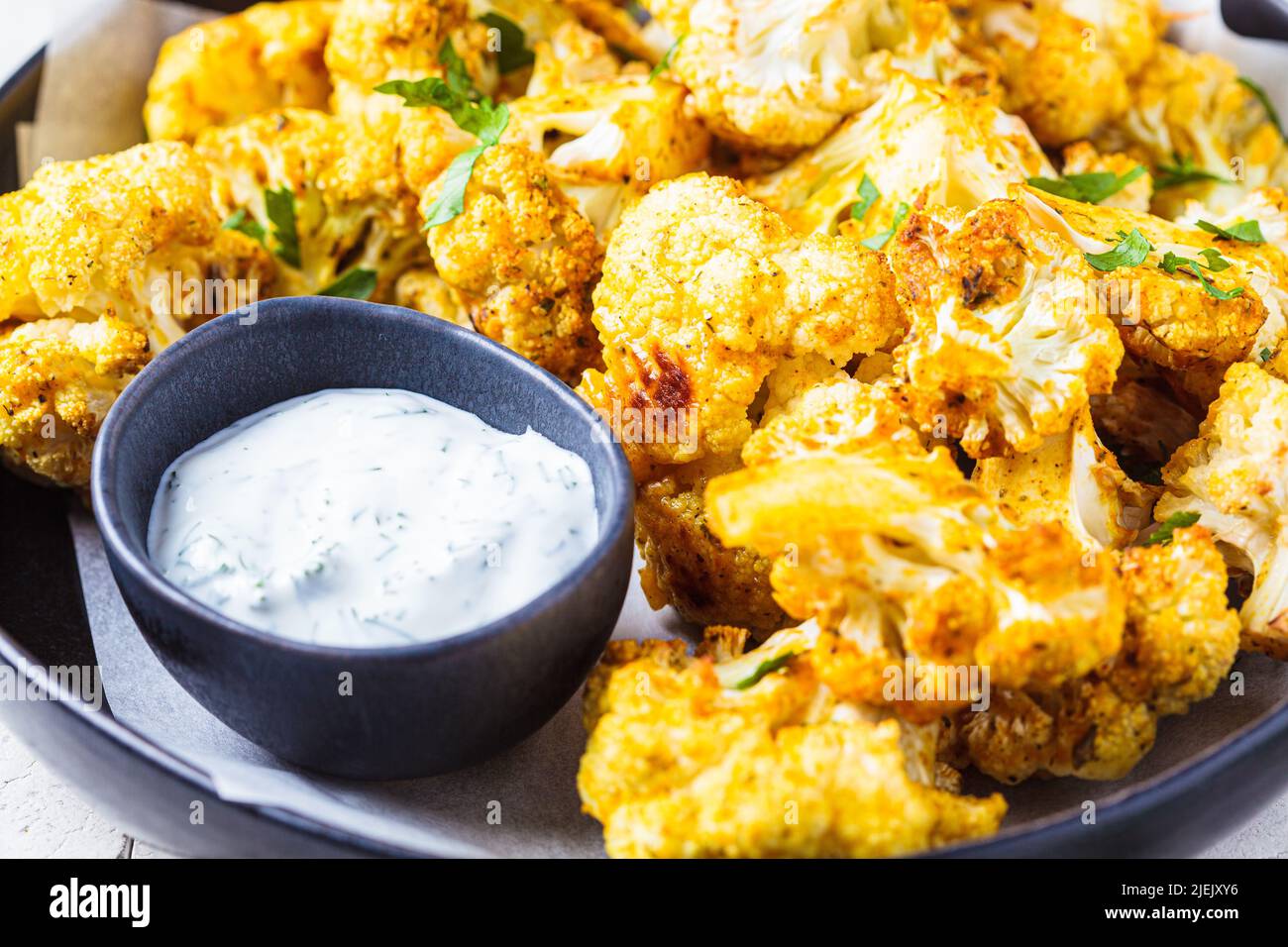 Ali di cavolfiore piccanti al forno con salsa di yogurt in un piatto nero. Concetto di ricetta di dieta vegana. Foto Stock