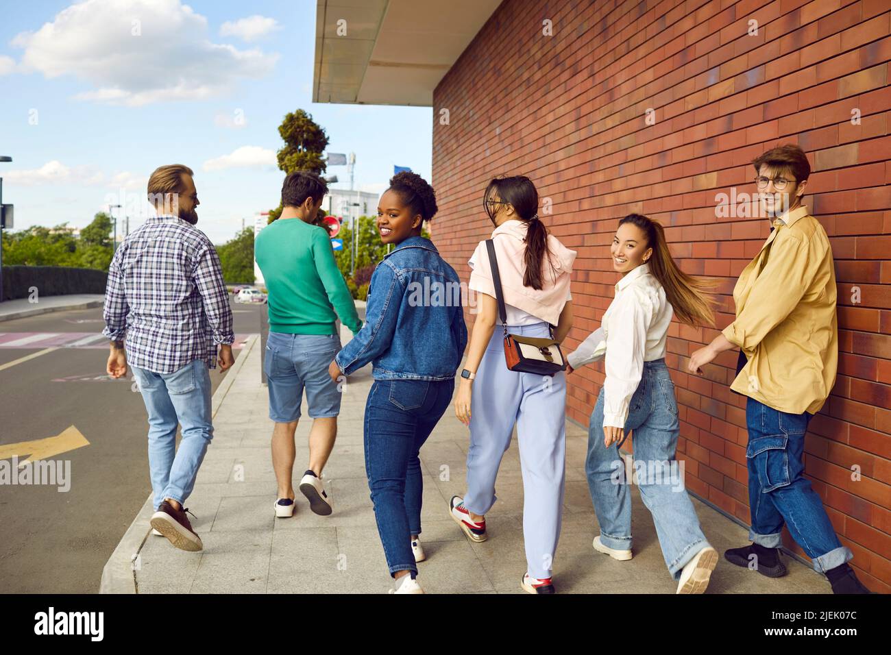 Gruppo di giovani amici multirazziali allegri guardano indietro mentre camminano sulla strada insieme Foto Stock