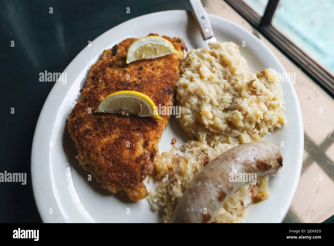 Schnitzel di maiale tedesco con un lato di crauti, una salsiccia bratwurst, e purè di patate su un piatto per la cena Foto Stock