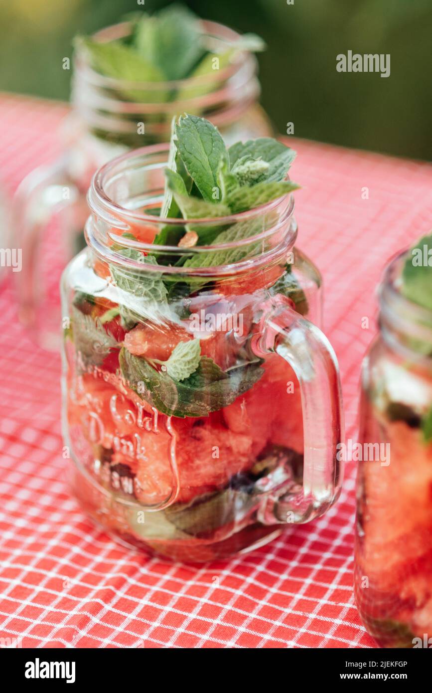 L'acquomelone e la menta hanno infuso l'acqua di disintossicazione. Limonata con ghiaccio e menta come bevanda rinfrescante estiva in vasetti. Bibite fredde con frutta. Rinfrescante succo d'estate rosso Foto Stock