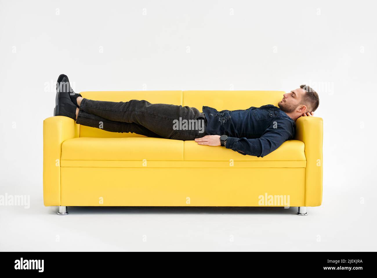 Il giovane uomo si rilassa da solo sul divano giallo di casa. Concetto REST Foto Stock