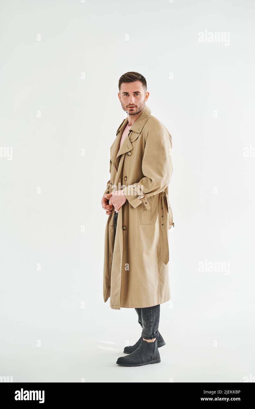 Ritratto a tutta lunghezza di giovane uomo alla moda in trench beige su sfondo bianco studio Foto Stock